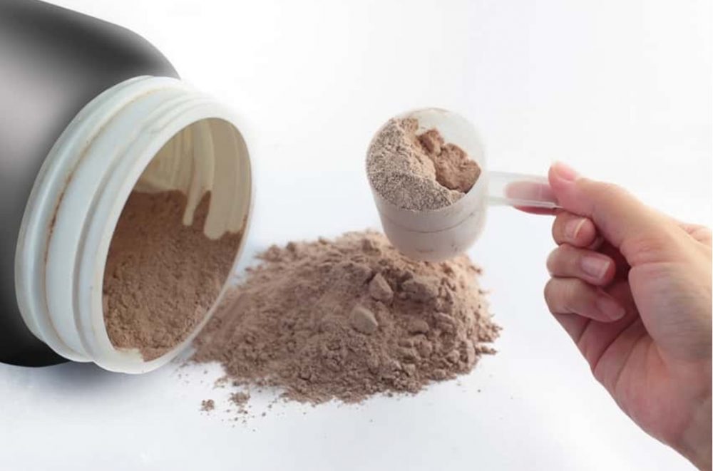 Bottle of protein powder with someone taking a scoop out
